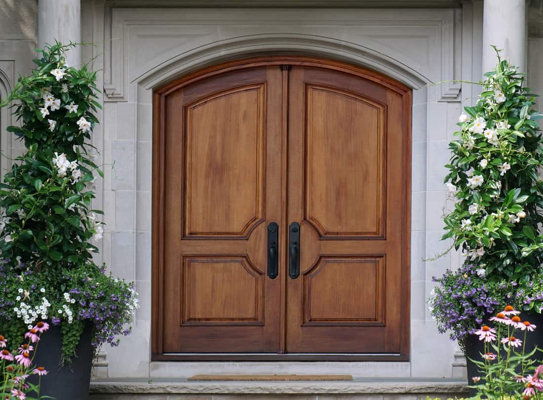Elegant wooden double front door with curved top, surrounded by flowers