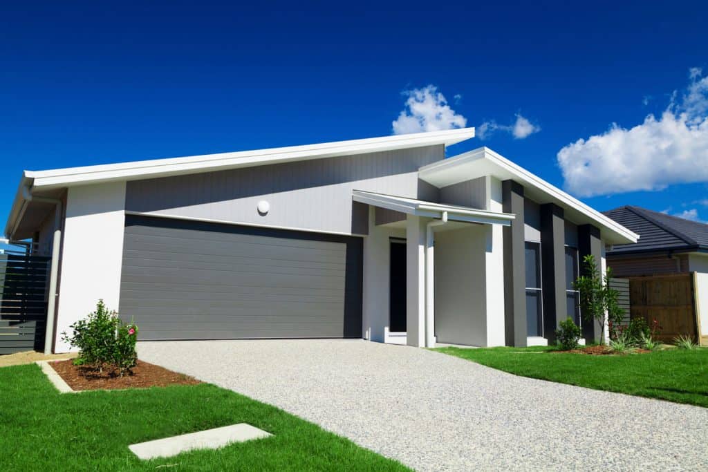 Exterior of a modern contemporary house with white painted walls, gray garage door, and pebble driveway