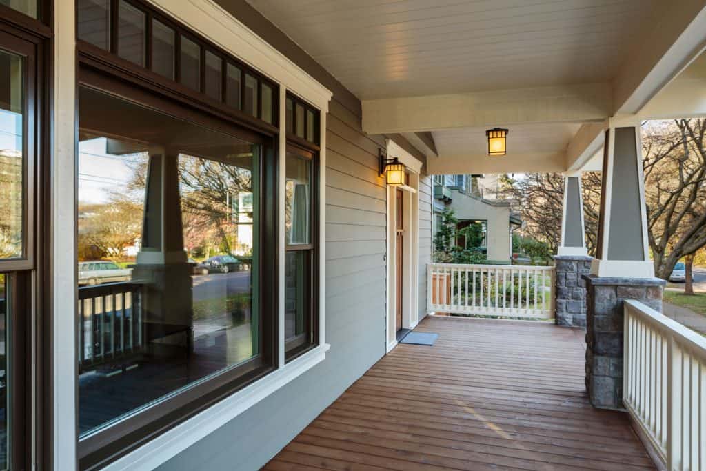 Front porch of a modern house with gray painted sidings, huge picture windows, and wooden flooring