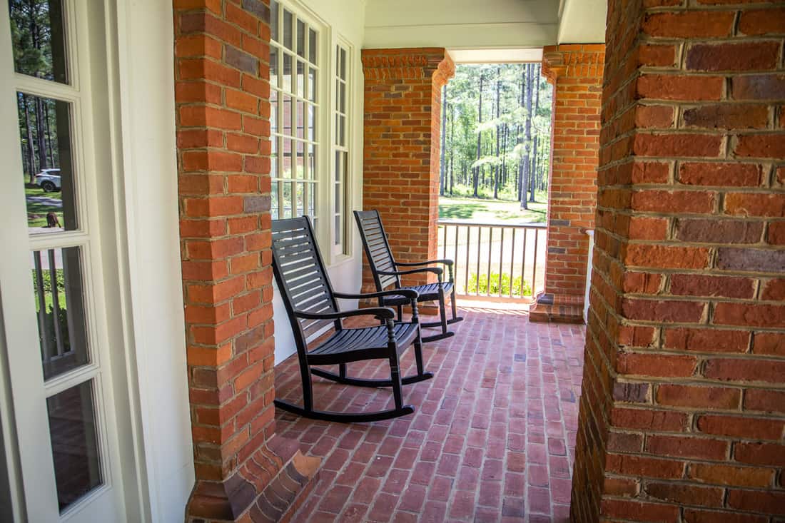 Front porch with rocking chairs. Exterior of Red Brick Traditional Southern Home.