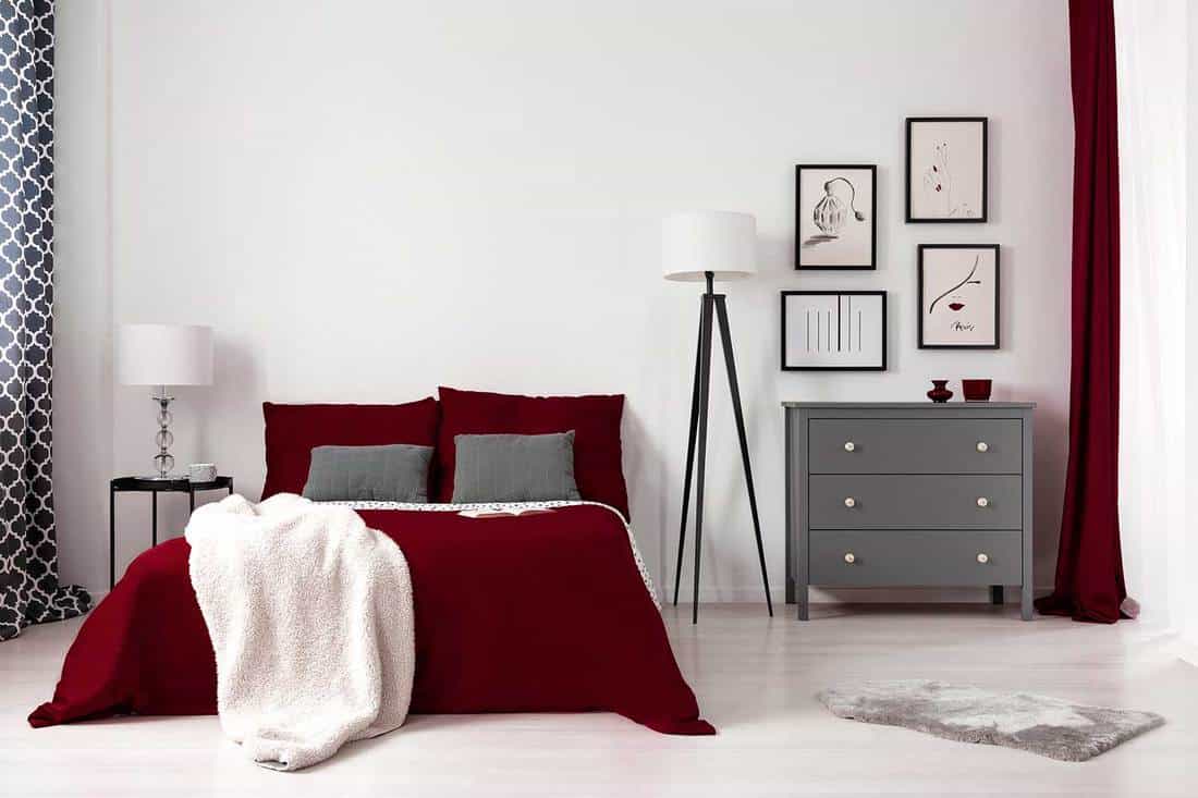 Glamour bedroom interior with dark red bed, blanket, lamp and gray commode