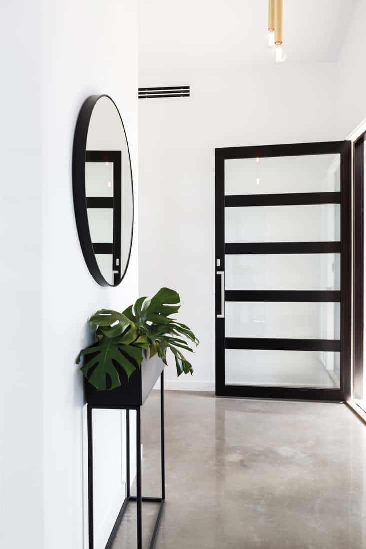 Glass entry door to foyer with circular mirror with a rectangular plant stand