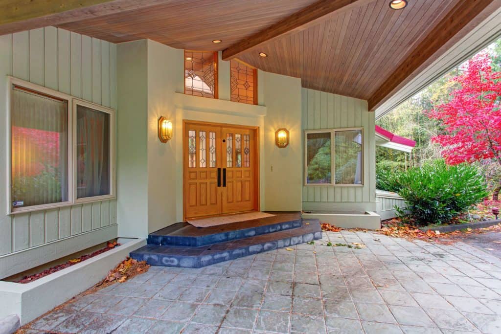 Green colored front porch with outdoor wall lamps, French front door, and wooden paneled ceiling