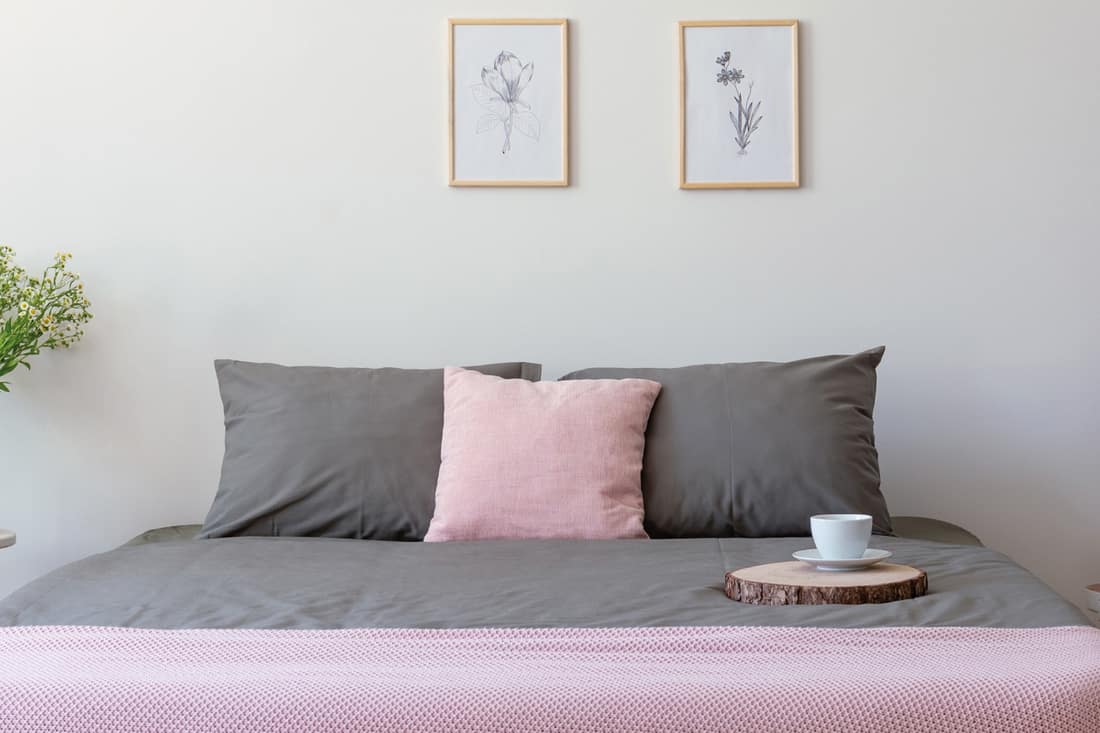 Grey and pastel pink bedding on double bed with coffee cup, fresh plants and simple posters