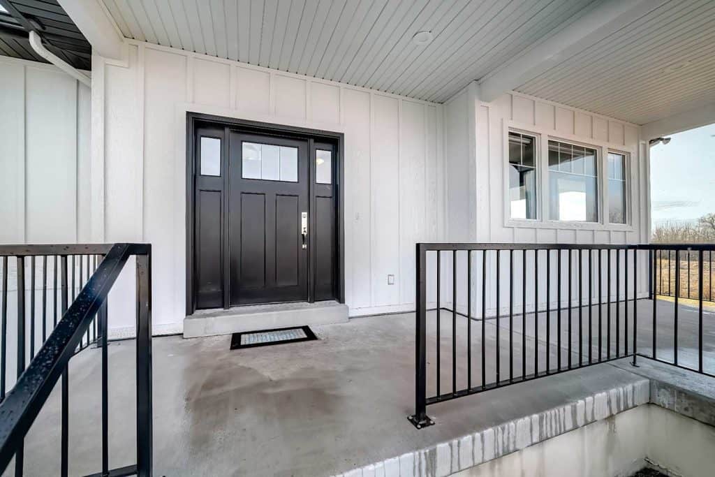 Home entrance with front porch and black front door against white paneled wall
