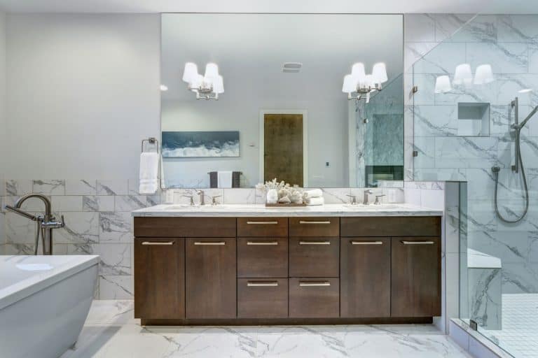 Incredible master bathroom with Carrara marble tile surround, modern glass walk in shower, espresso dual vanity cabinet, frameless mirror and a freestanding bathtub, How To Hang A Frameless Mirror [2 Different Techniques]