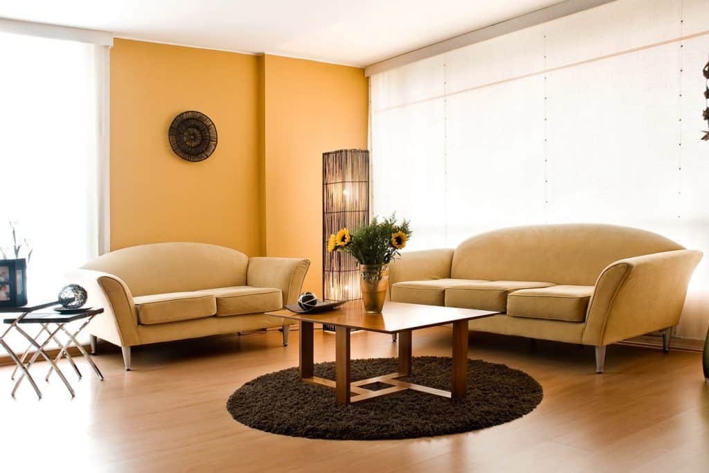 Interior of a beige themed living room with beige sofas, brown wooden coffee table, and brown wooden flooring