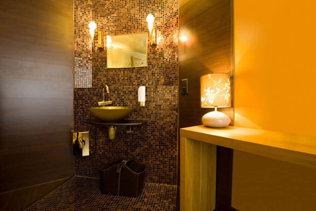 Interior of a luxurious orange themed bathroom wtih a decorative tiles on the shower area and a small lamp on top of a table