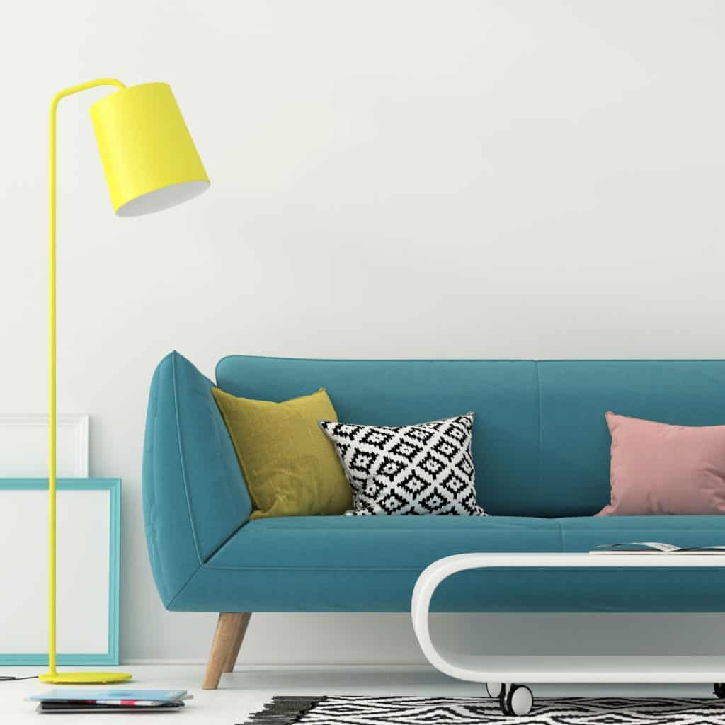 Interior of a minimalist themed living room with a blue sleeper sofa, yellow floor lamp, and white walls