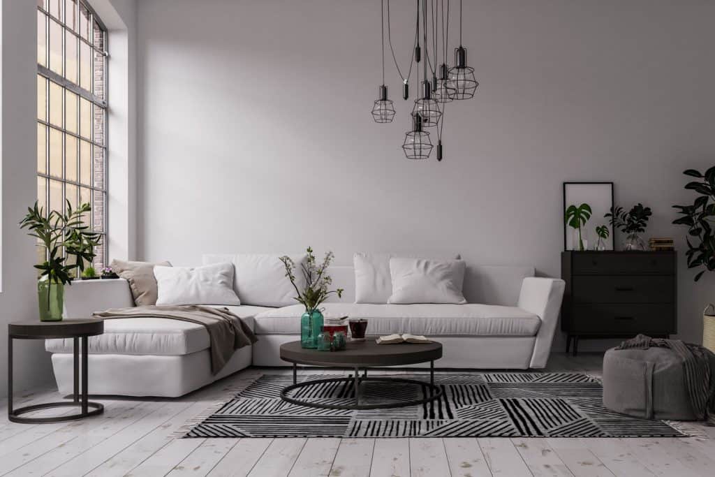 Interior of a modern industrial themed living room with dark colored furniture's industrial chandelier, and a gray ottoman with a checkered drape
