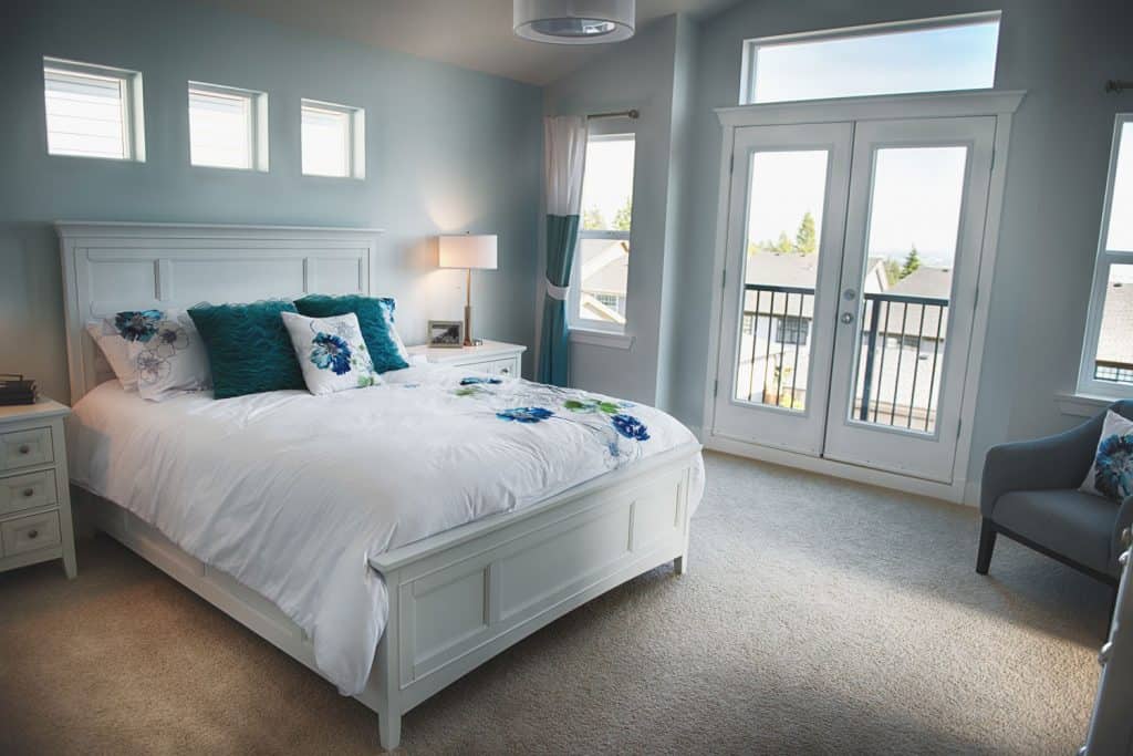 Interior of a small teal and contemporary bedroom with a carpeted flooring, white French door leading to the balcony, and blue painted walls