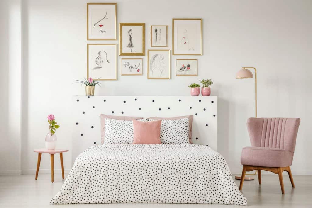 Interior of an elegant bedroom with white polka dot beddings, pink side chair, and mock picture frames on the wall