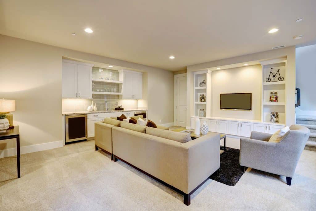 Interior of an open space living room with beige painted walls, square arm sofas, and large tv section with cabinets on the side