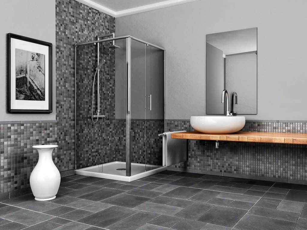Grande salle de bain avec carrelage gris, miroir au-dessus du lavabo et douche avec portes vitrées