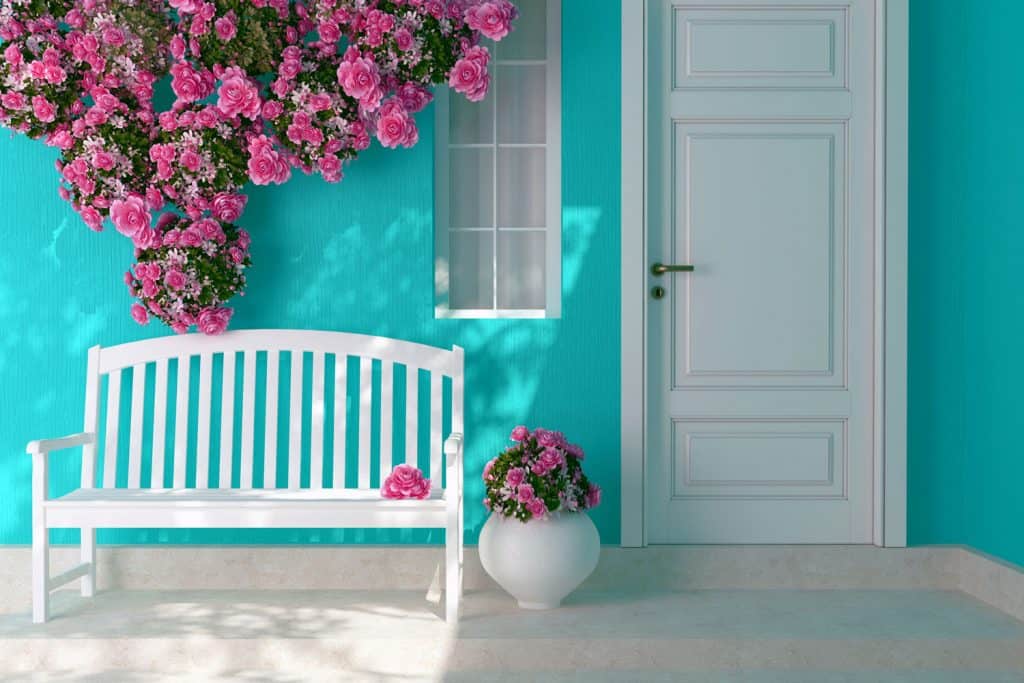 Light blue painted front porch wall with a pink flowers on the wall and a white bench
