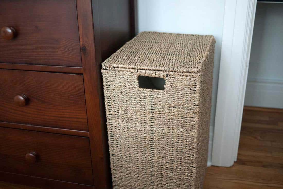 Light brown wicker laundry basket beside a wooden dresser in a bedroom