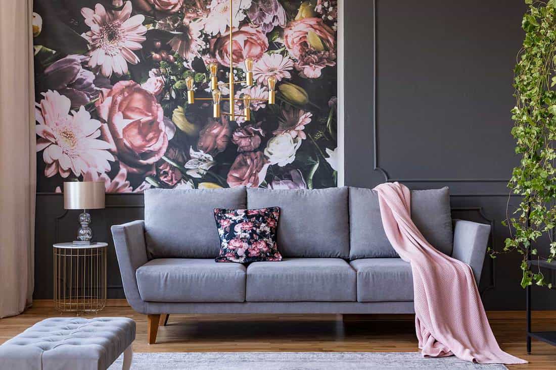 Living room interior with a sofa, pillow, blanket and flowers on wallpaper