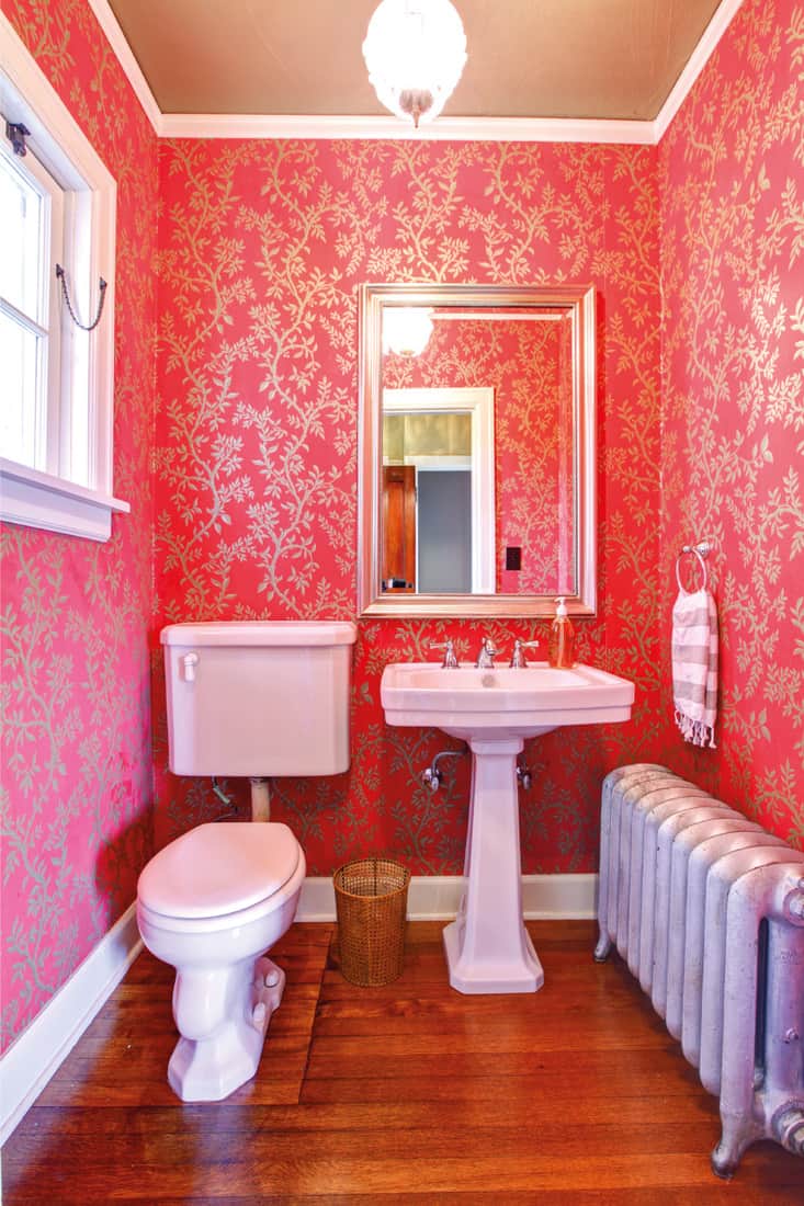 Petite salle de bains de luxe rouge et or avec radiateur argenté.  papier peint autour d'un évier