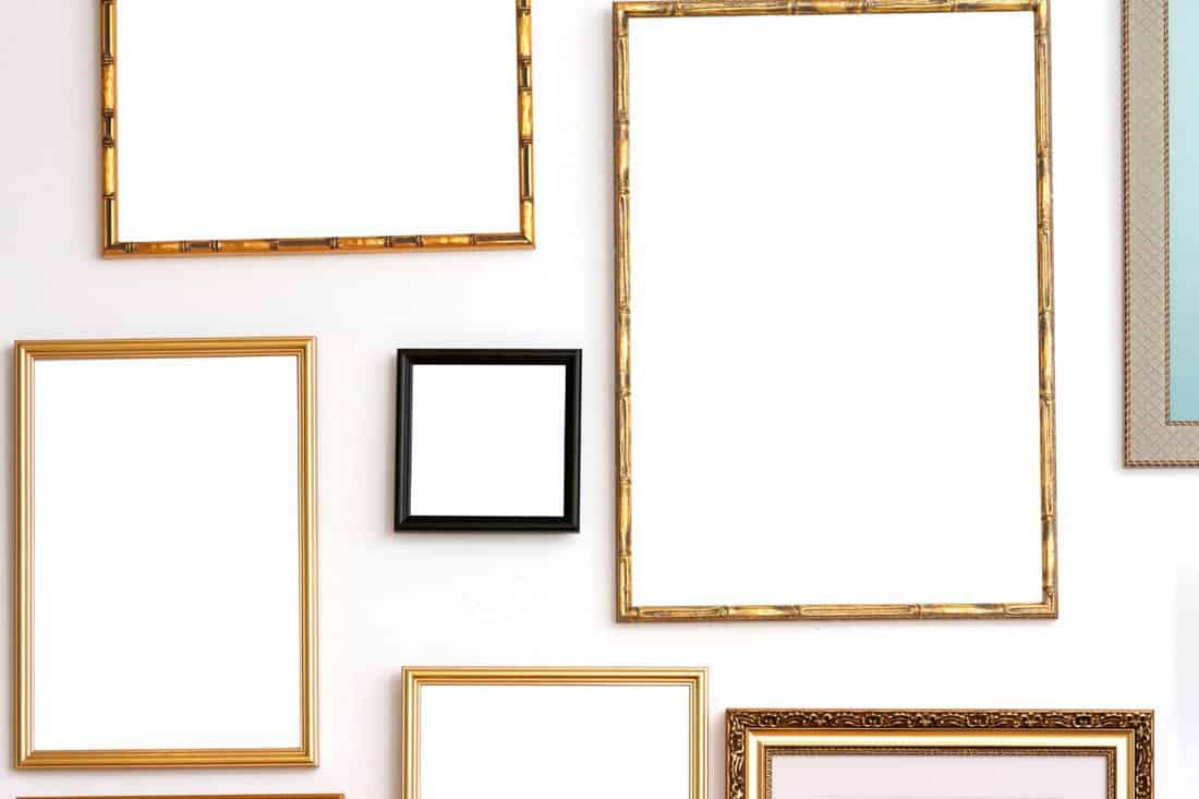 Maximalist gallery wall mockup with classic, vintage-style mismatched golden picture frames. Blank frames on a white wall.