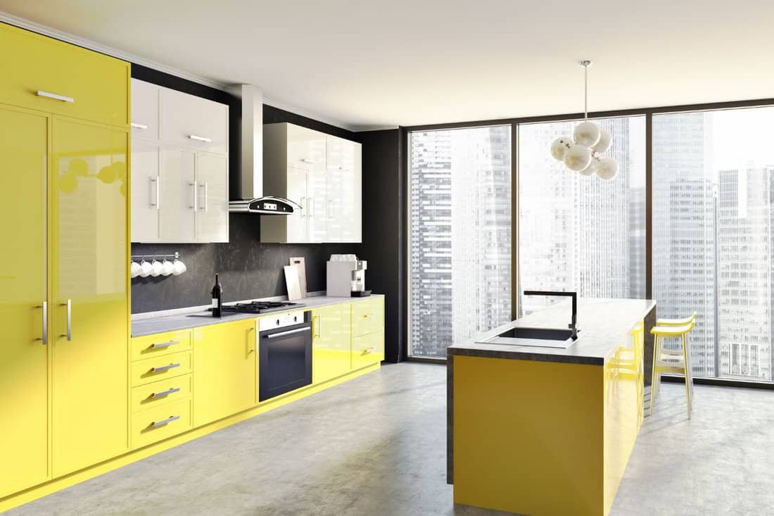 Modern kitchen corner with yellow and white counters, a table and two stools. Black walls and a concrete floor. 