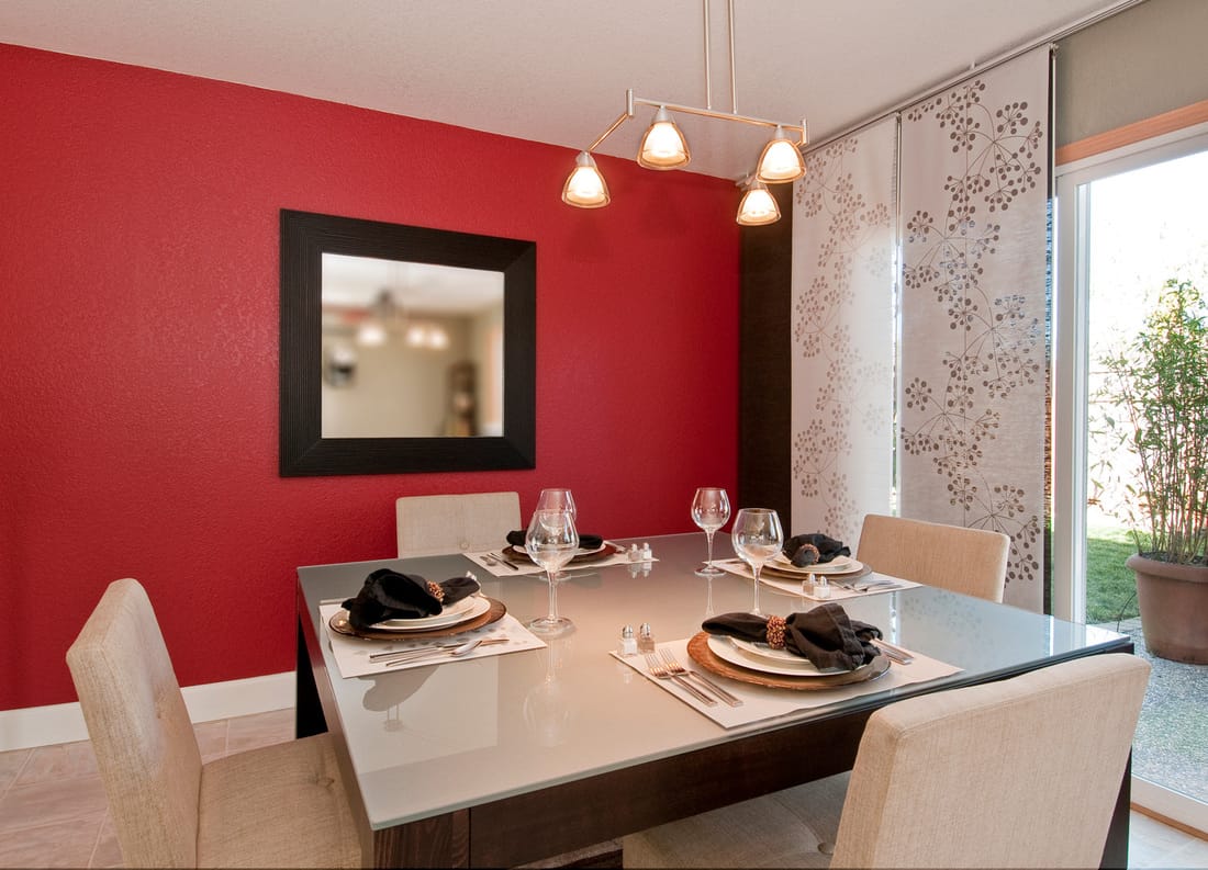 Modern kitchen with four seater table, red walls and white curtains