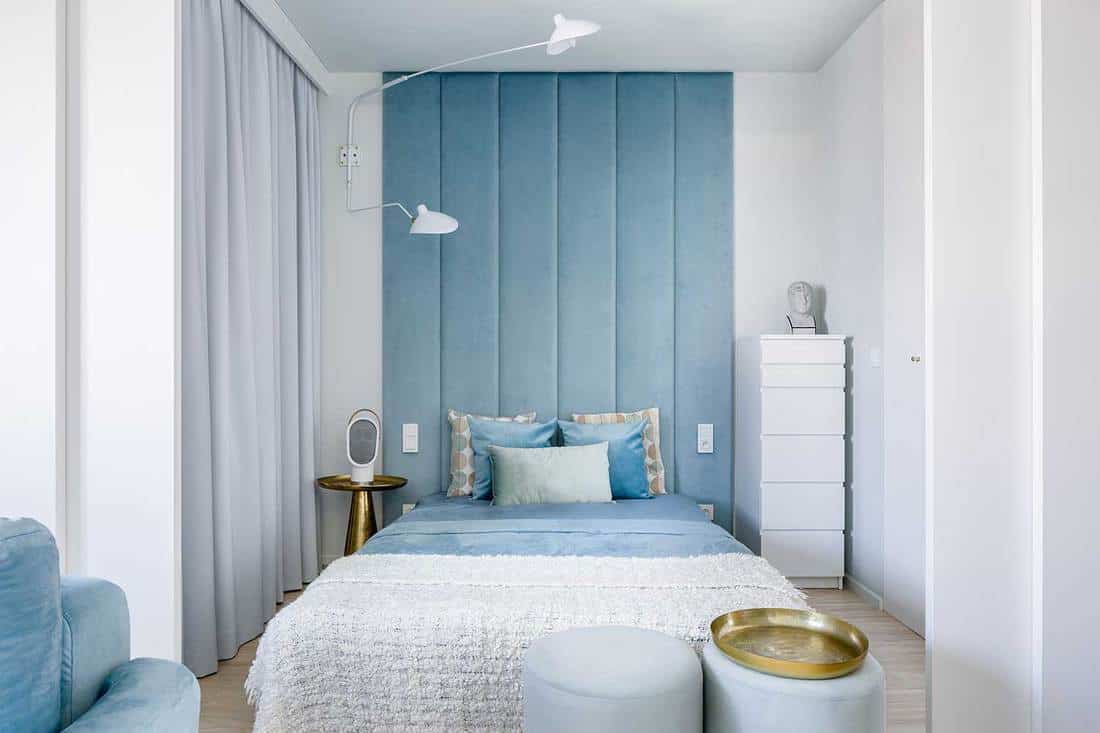 Narrow blue and gray bedroom with double bed and upholstered wall