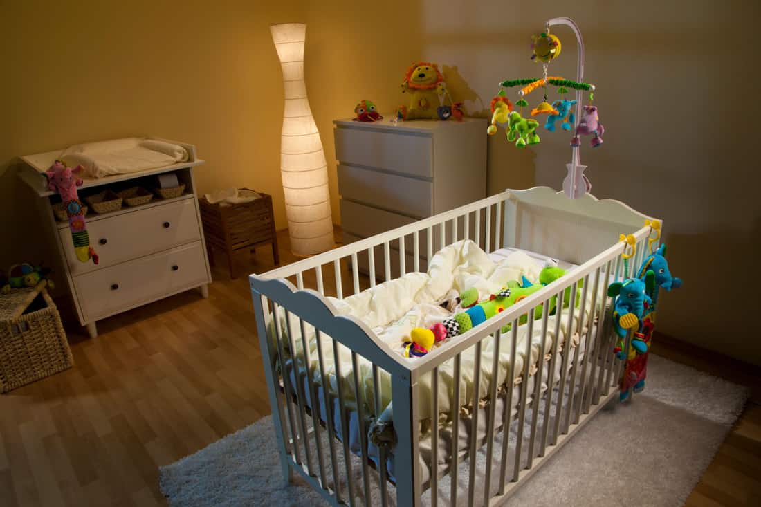 Chambre d'enfant éclairée par une lampe et décorée avec des meubles modernes et de nombreux jouets doux pour bébé, quelle couleur de veilleuse convient le mieux aux bébés ?
