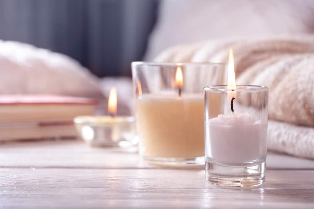 Several candles in glasses on white wooden table in front of bed