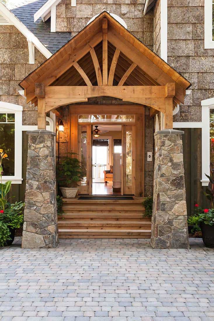 Stone and wood front porch entryway to upscale country house with open front door and paving stone driveway