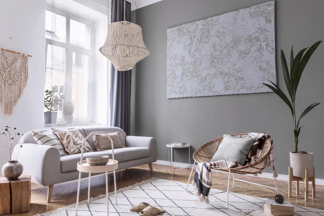 Stylish composition of creative and cozy living room interior with grey sofa, coffee table and rattan armchair