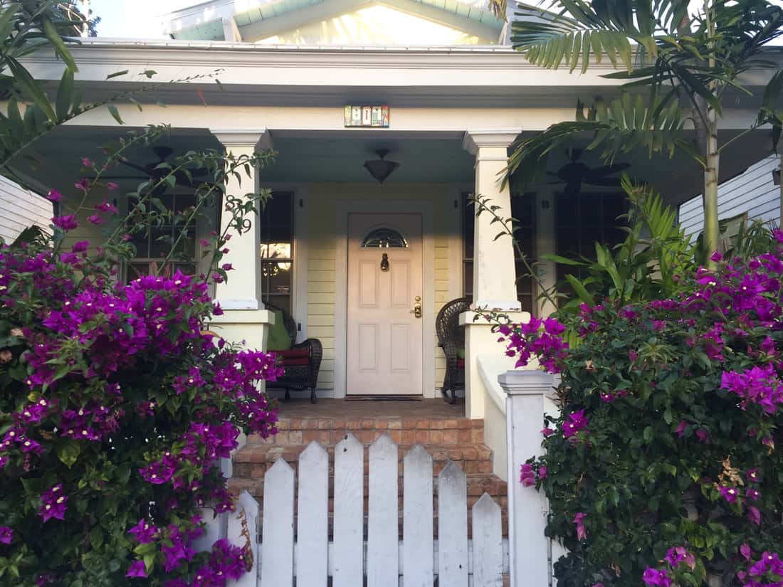 The quaint conch-style architecture with large front porch, white siding and lush tropical gardens