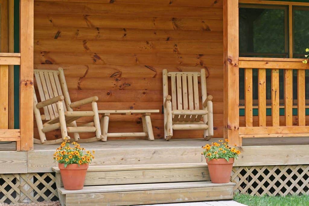Two wood rocking chairs on a porch with flowers on the steps
