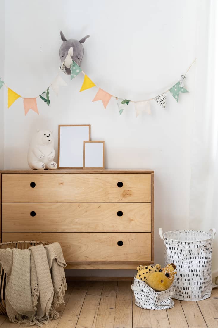 Vertical photo of cozy child bedroom with authentic interior design, flags on wall, home decor in wicker basket, toys on wooden chest of drawers