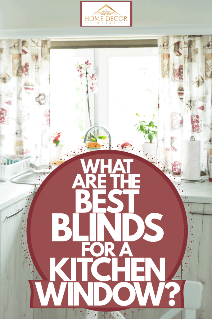 Interior of a small white themed kitchen with floral blinds on the window and indoor plants on the windowsill, What Are The Best Blinds For A Kitchen Window?