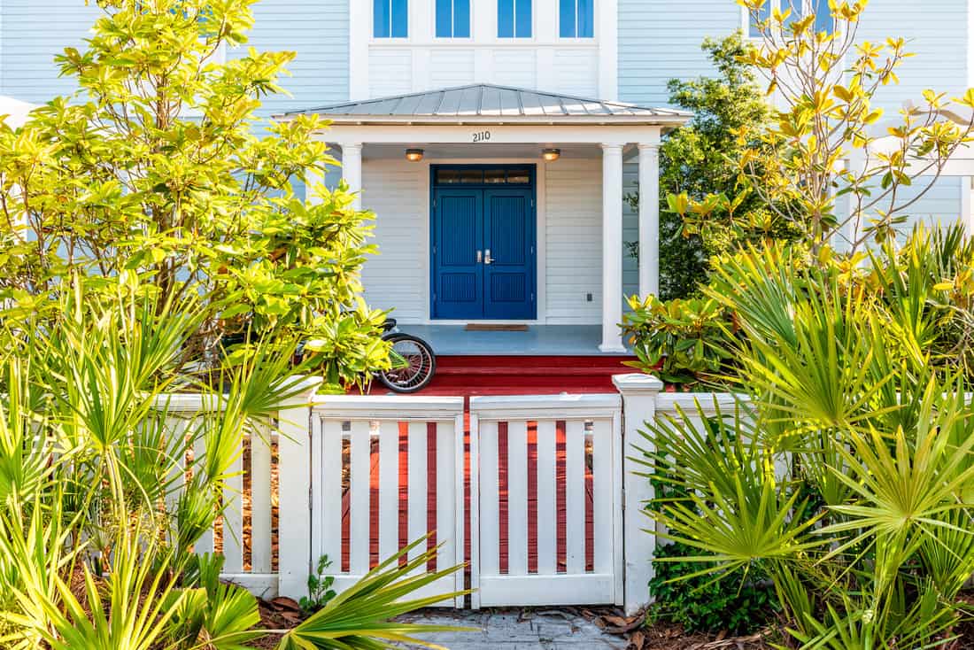  White and blue beach wooden wood architecture of house and door gate to front porch yard with green landscaping plants bicycle vacation cottage home fence