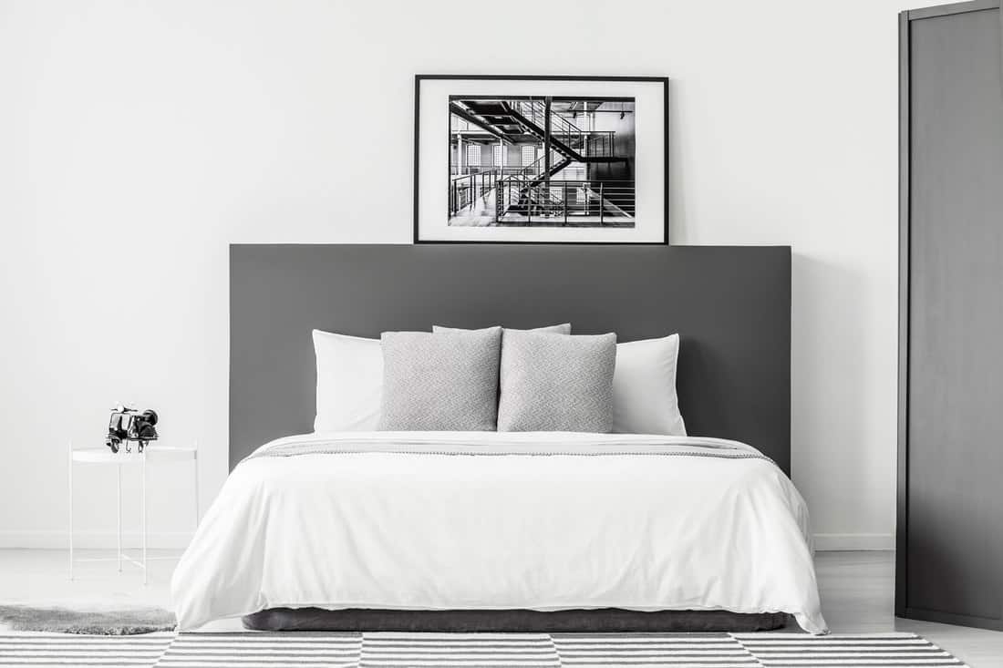 White bed with grey bedhead in minimal bedroom interior with poster and round table