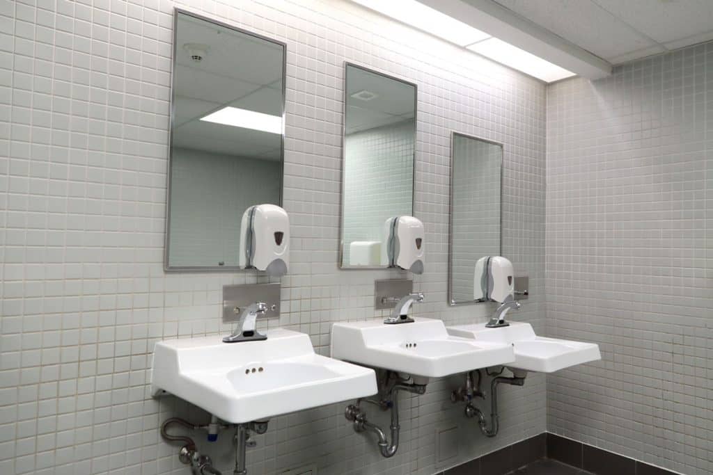 White lavatories and wall mounted soap dispensers with mirrors inside a public bathroom