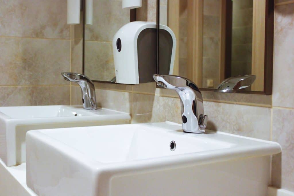 White sinks inside a modern bathroom with a wall mounted soap dispenser
