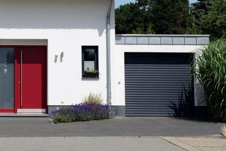 White two-story house features a black roof and a roll up black garage door, How To Paint A Roll Up Garage Door [9 Simple Steps]
