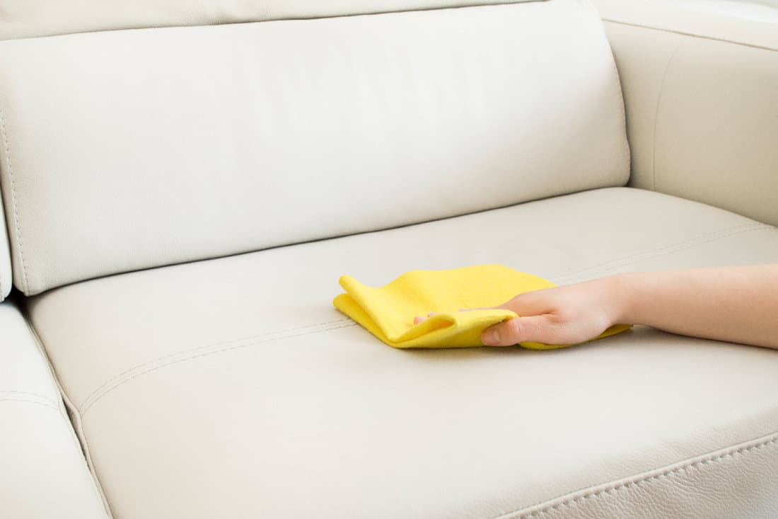 Woman cleaning a beige sofa with yellow cloth