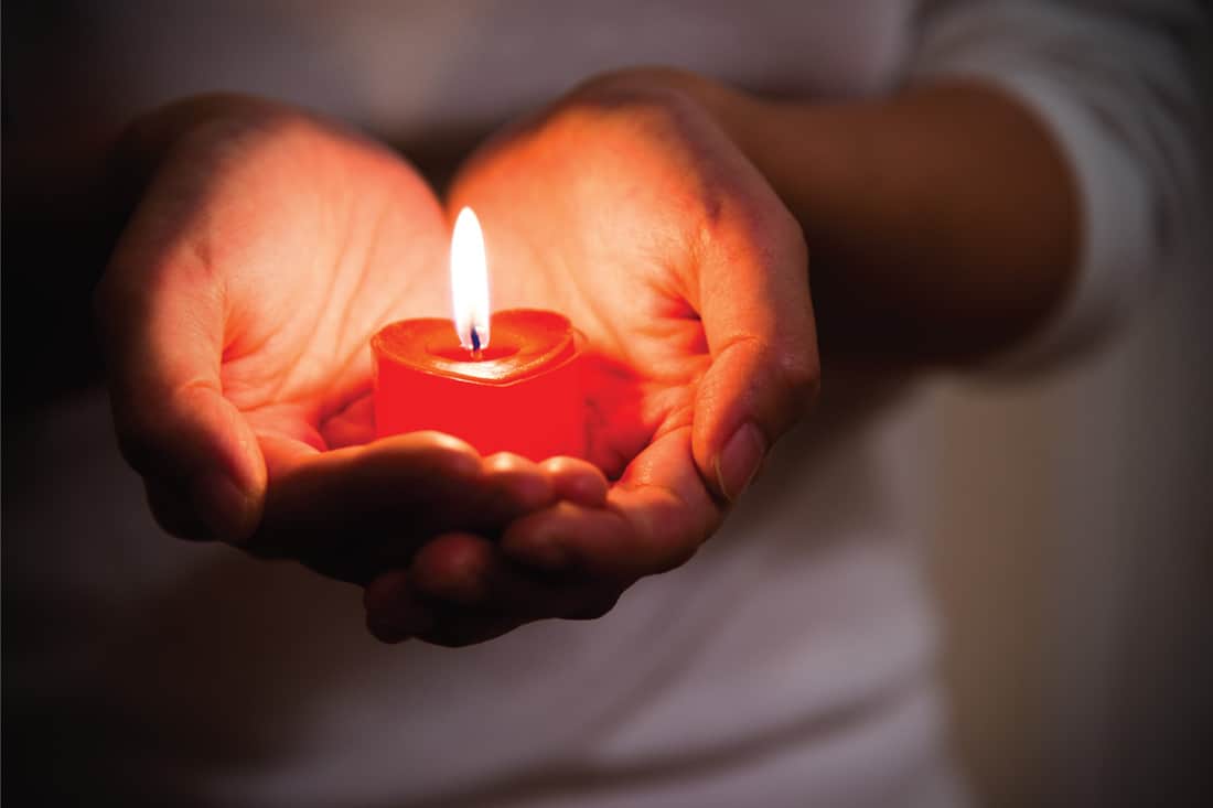 Woman hands holding burning heart-shaped candle. Symbol of hope, peace and love.