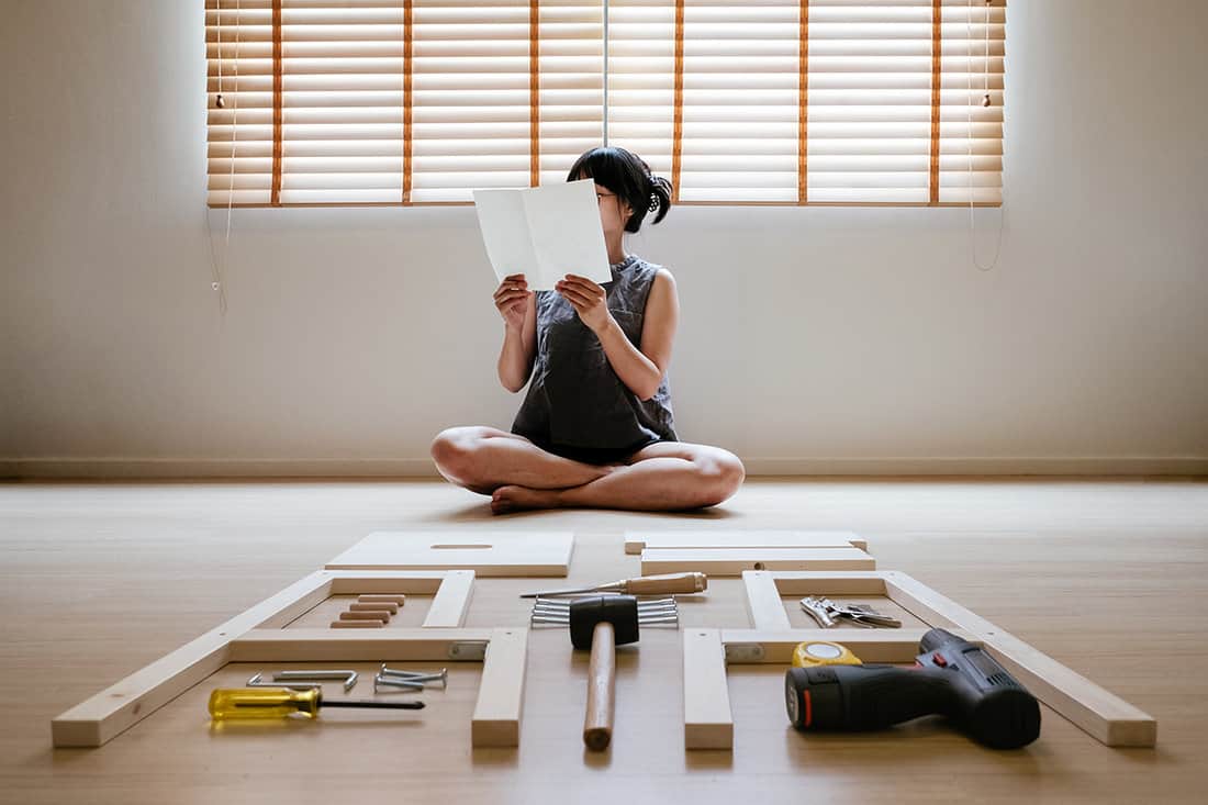 Woman self assembly wooden furniture and read blank white paper to put instruction