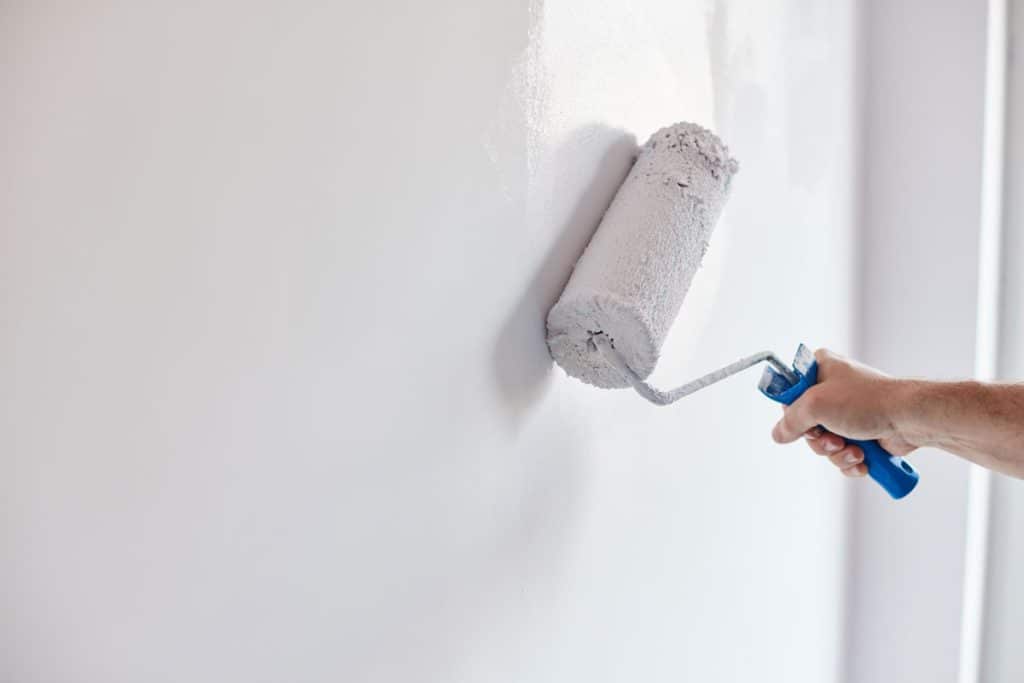 Worker painting the walls with white paint