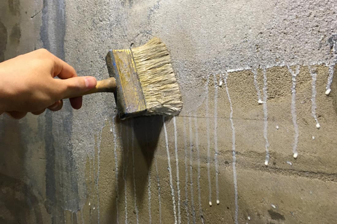 Worker's hand in a glove with a brush primers a concrete wall