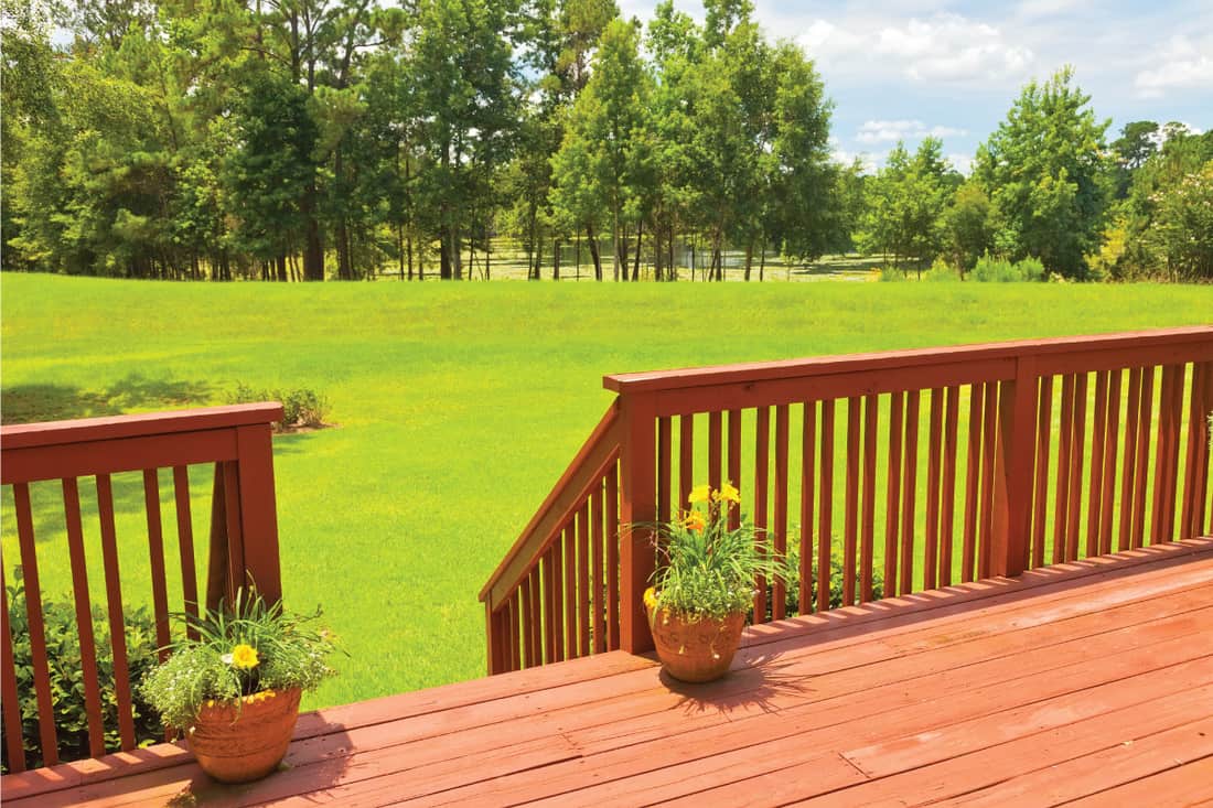 backyard wood deck with wood railing, green backyard, tree line. 11 Incredible Deck Railing Style Ideas