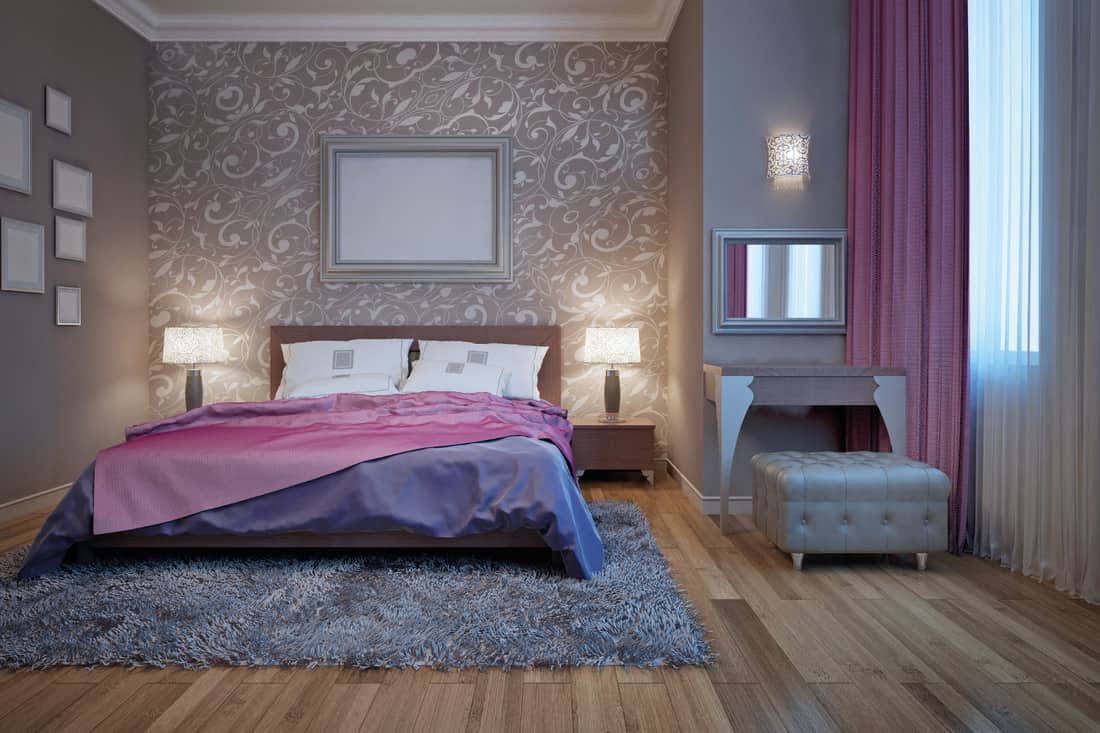 Bedroom with dressing table, gray ottoman, carpet, frames, wallpaper, pink blanket, gray bedsheet
