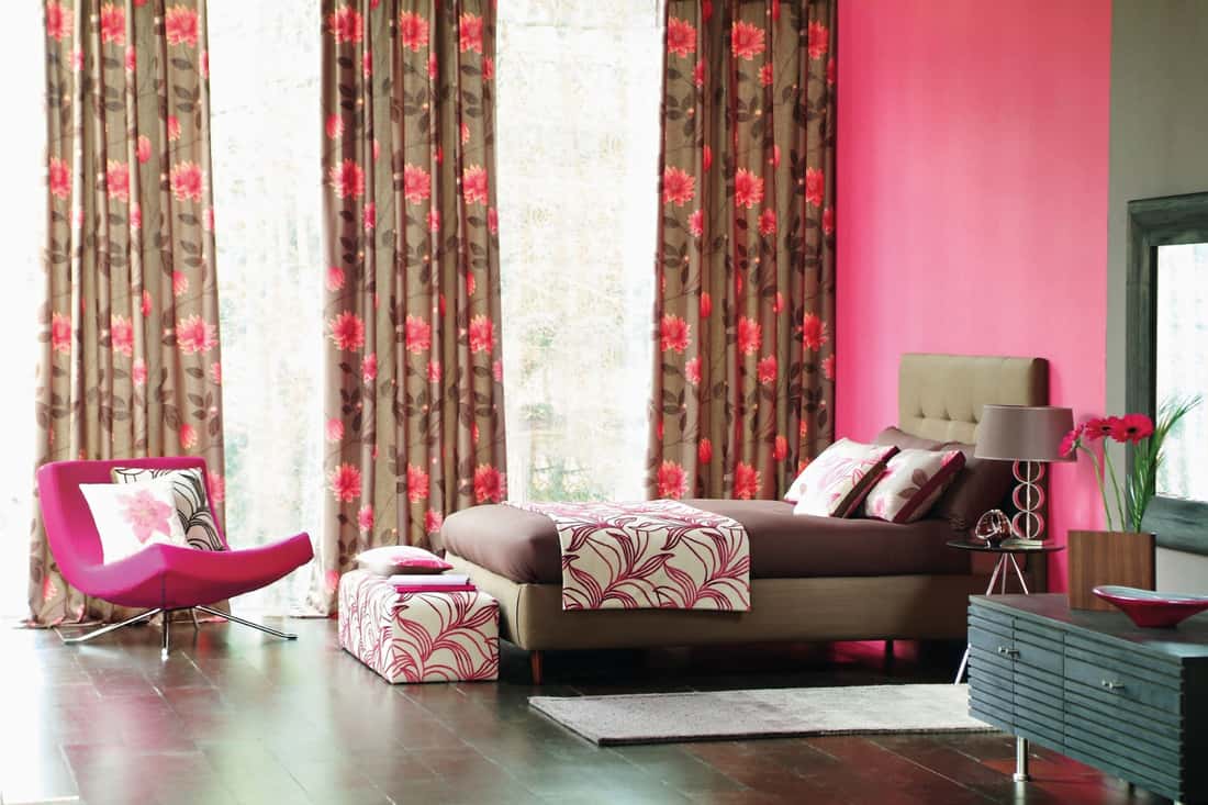 Chambre à coucher avec de longs rideaux fleuris, lit marron, canapé rose