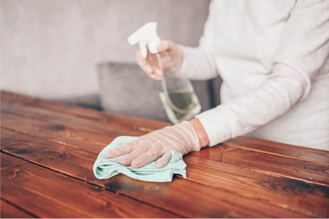 cleaning home wood table, sanitizing kitchen table surface with disinfectant antibacterial spray bottle, washing surfaces with towel and gloves. How To Disinfect Wood Furniture Without Damaging The Finish