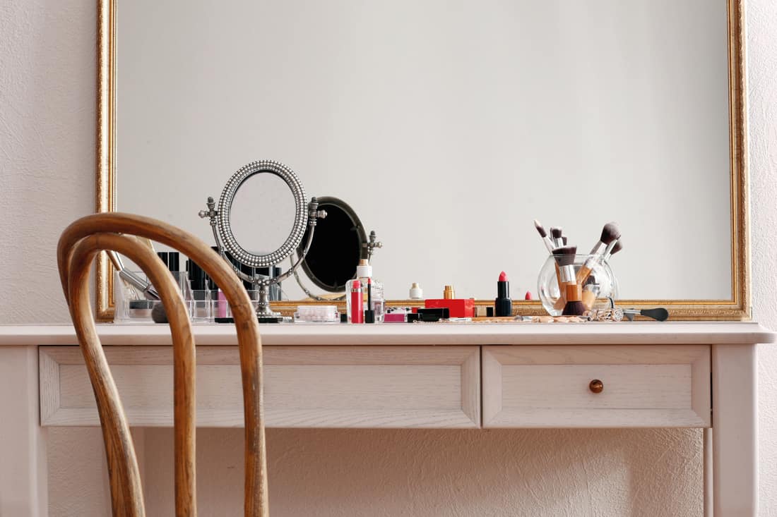 Cosmetics on a dressing table with a large mirror and a wooden chair