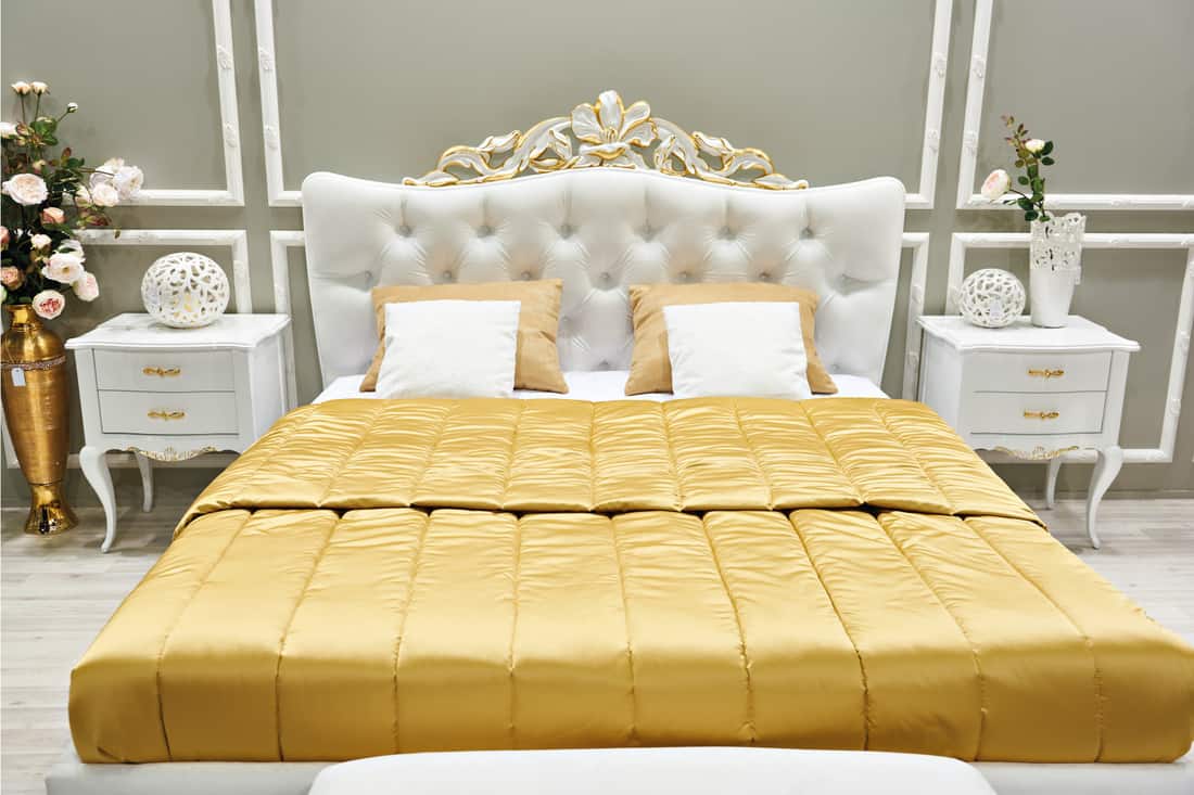 Gray bedroom with white bed frame and headboard, gold bedding and white nightstands